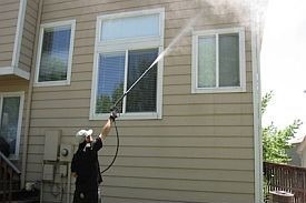 Man pressure washing vinyl siding on house.